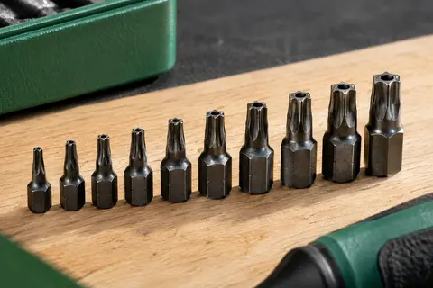 Dix embouts Torx noirs de T3 à T20 alignés sur un établi en bois clair